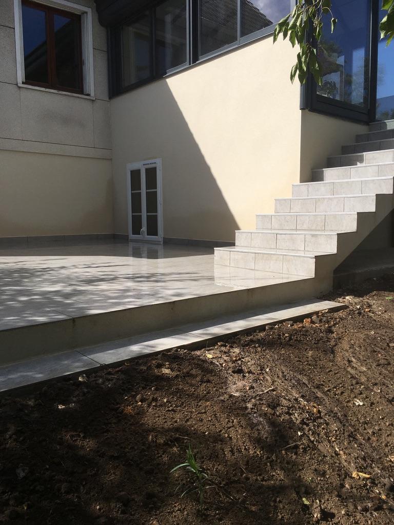 Terrasse au pied d'une véranda surélevée, accessible par des escaliers