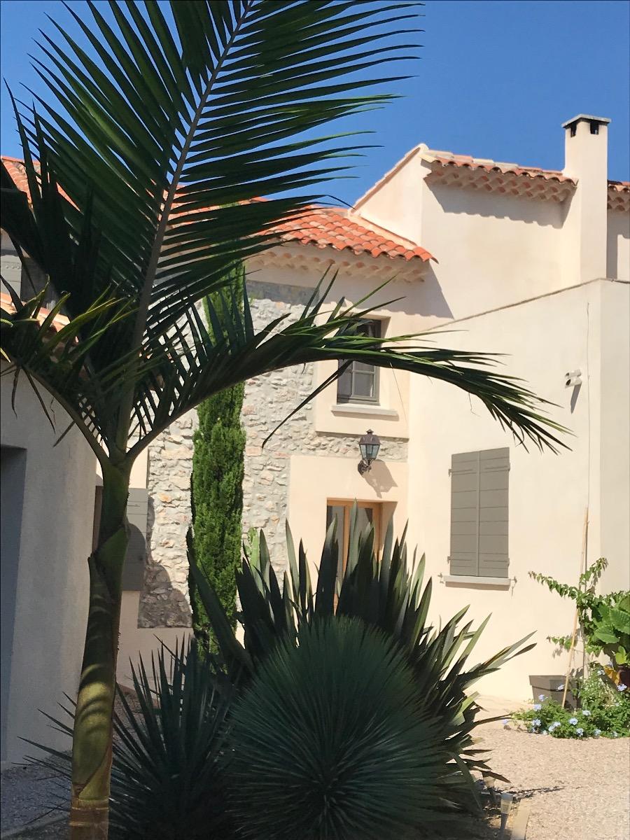 Maison avec façade en pierre, volets gris, toit en tuiles et végétation