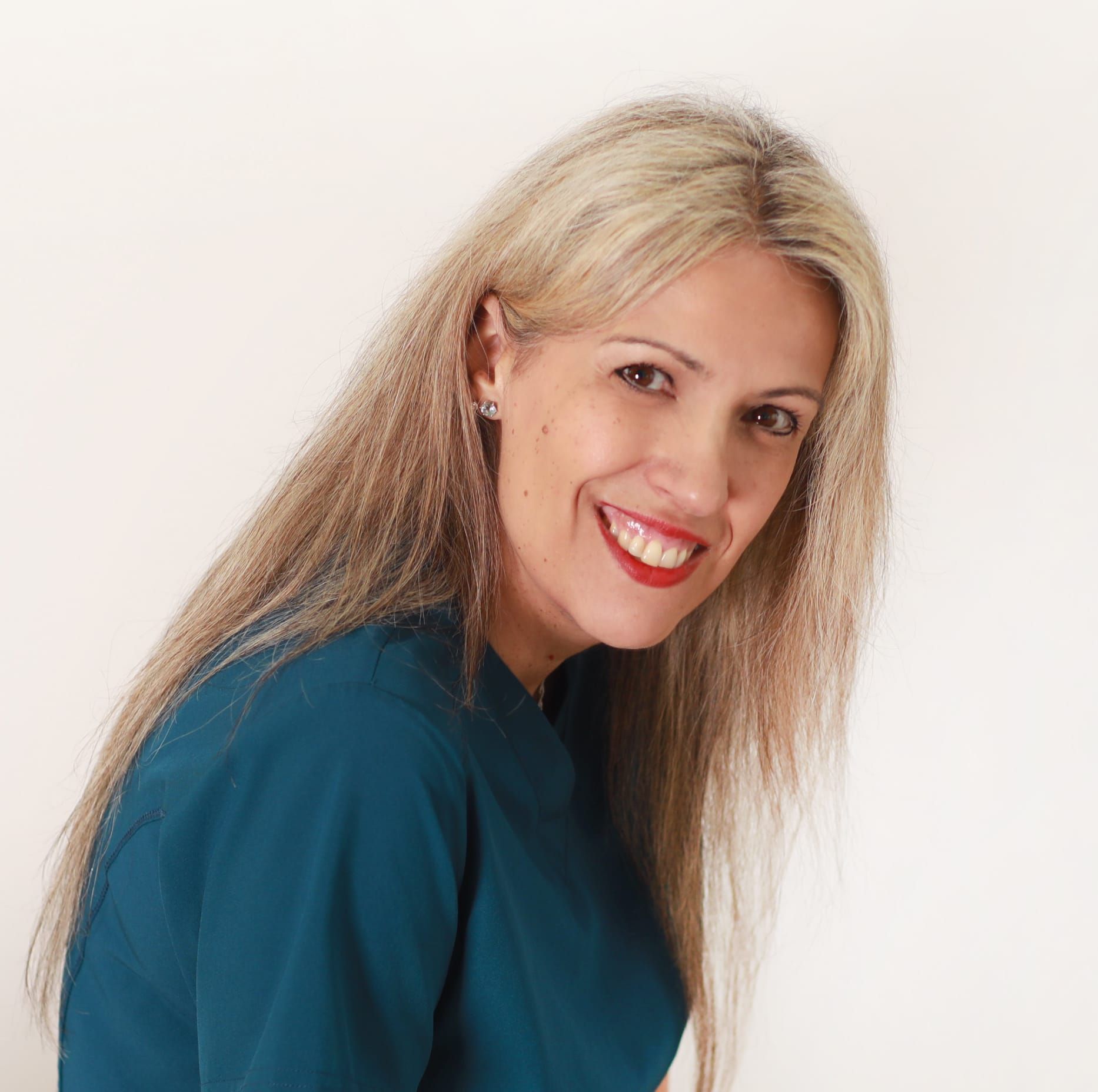 Mujer sonriente con camisa morada de pie sobre fondo blanco con los brazos cruzados.