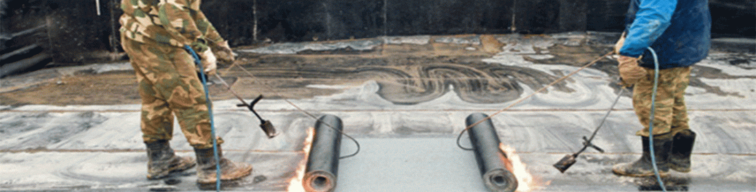 Deux ouvriers utilisent des chalumeaux pour poser des matériaux de toiture sur une surface humide.