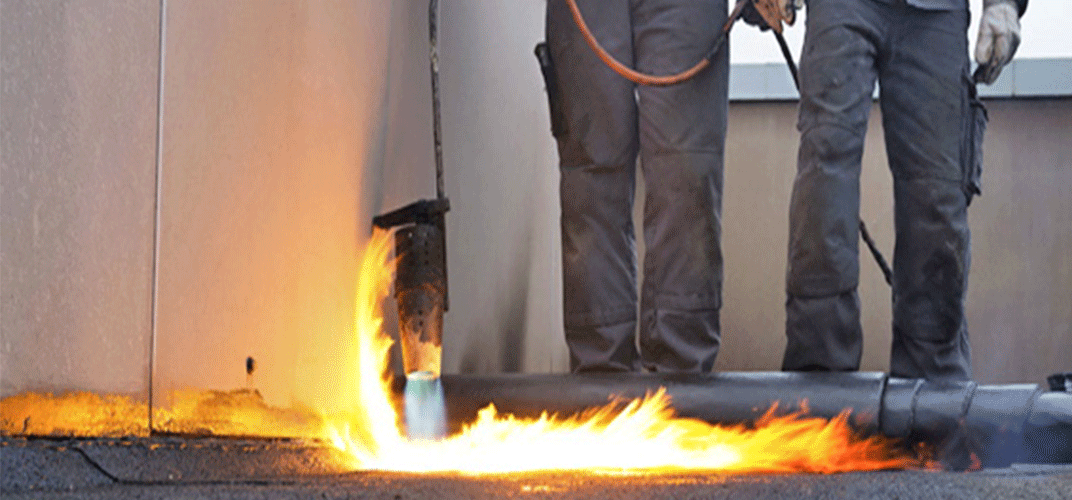 Des ouvriers utilisent une torche pour sceller les matériaux de toiture à l'aide de grandes flammes.