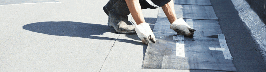 Personne portant des gants installant des bardeaux de toiture sur un toit plat.