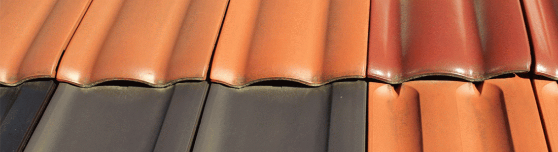 Gros plan sur un toit de tuiles, montrant l'alternance de tuiles orange et gris foncé.