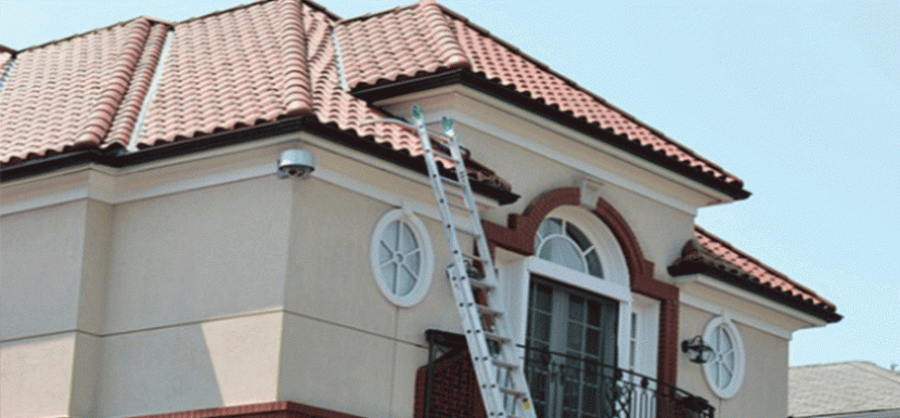 Échelle appuyée contre une maison en stuc beige clair avec un toit de tuiles rouges.