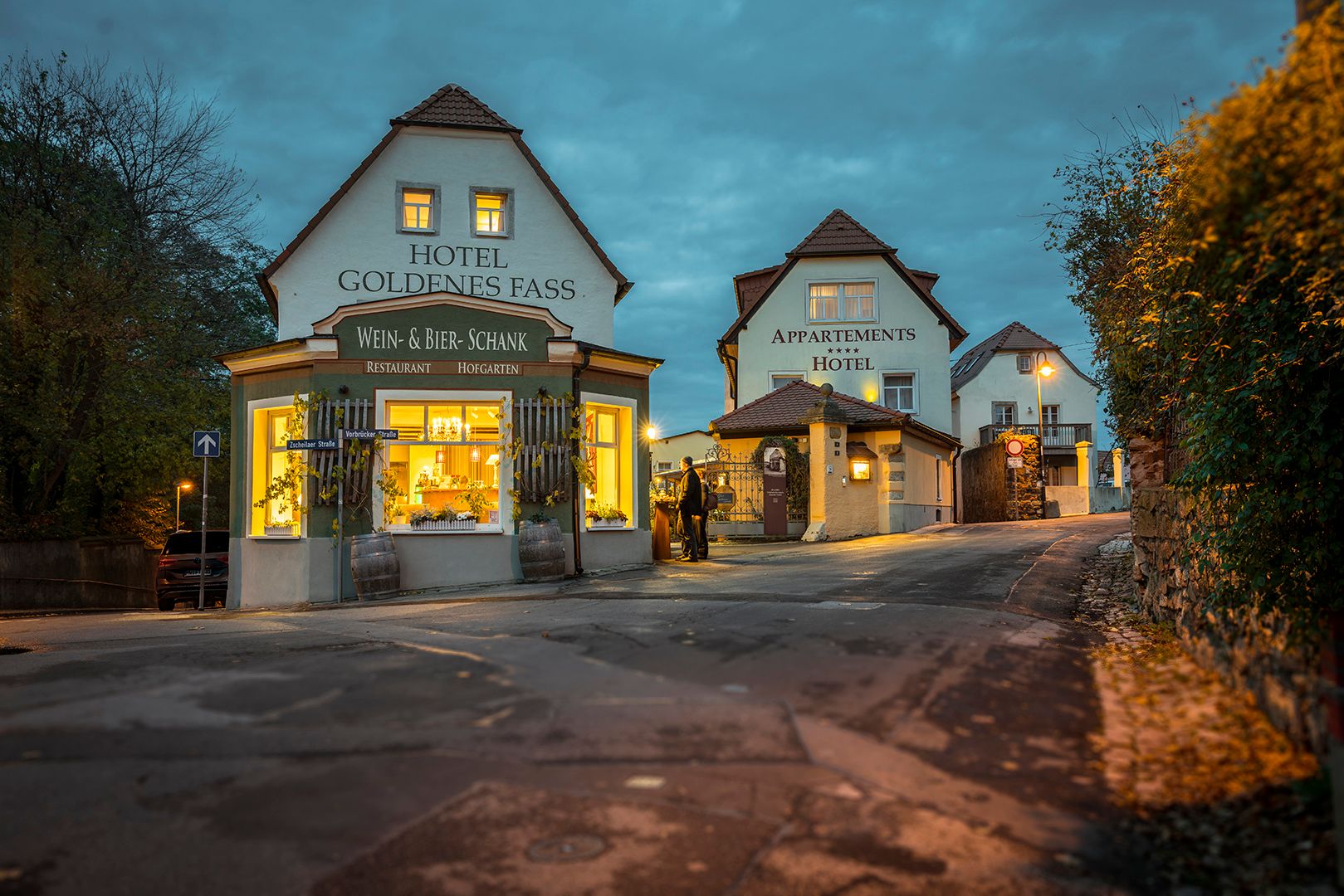 Hotelgebäude mit beleuchteter Schaufensterfront und Straße in der Abenddämmerung.