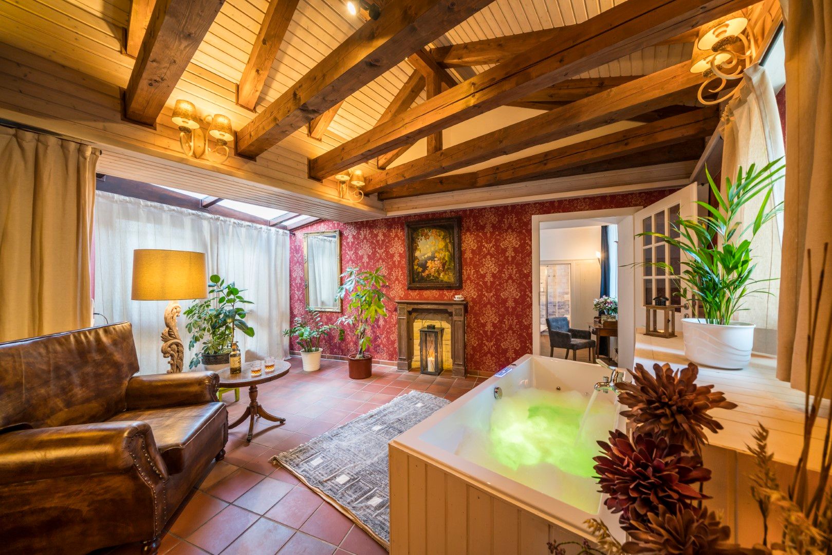 Gemütliches, spa-ähnliches Zimmer mit beleuchtetem Whirlpool, roter Tapete, Holzbalken und einem Ledersessel.