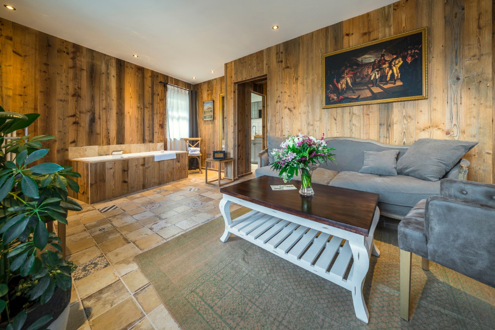 Wohnzimmer mit holzgetäfelten Wänden, grauem Sofa, Blumenarrangement und weißem Couchtisch.