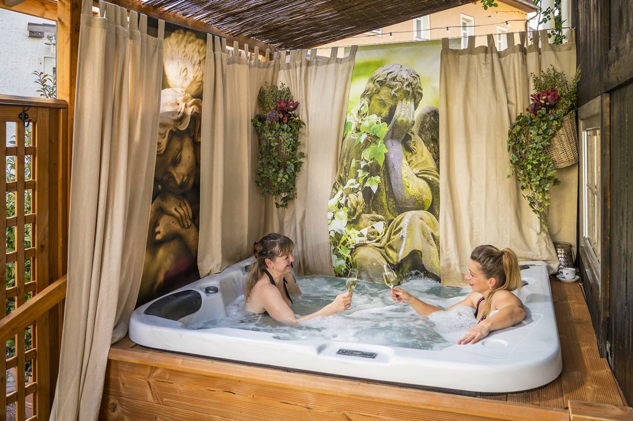 Zwei Frauen entspannen sich in einem Whirlpool unter einem Baldachin. Vorhänge und Kunstwerke an den Wänden.
