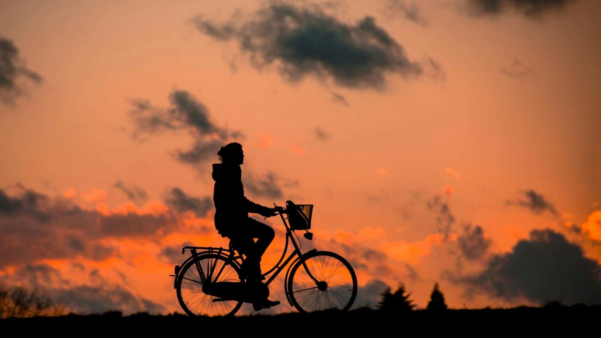 Silhouette eines Radfahrers, der bei Sonnenuntergang vor einem orangefarbenen, bewölkten Himmel fährt