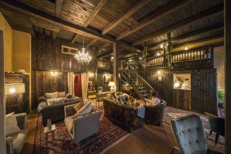 Gemütliches, rustikales Wohnzimmer mit Ledersesseln, Kronleuchter, gemustertem Teppich und einer Treppe im Hintergrund