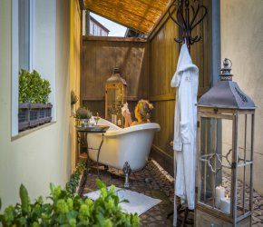 Frau entspannt in einer freistehenden Badewanne auf einer rustikalen, überdachten Terrasse mit Laternen und Pflanzen