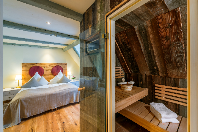 Schlafzimmer mit zwei Betten neben einer offenen Tür zu einer Holzsauna, warm beleuchteter Innenraum.