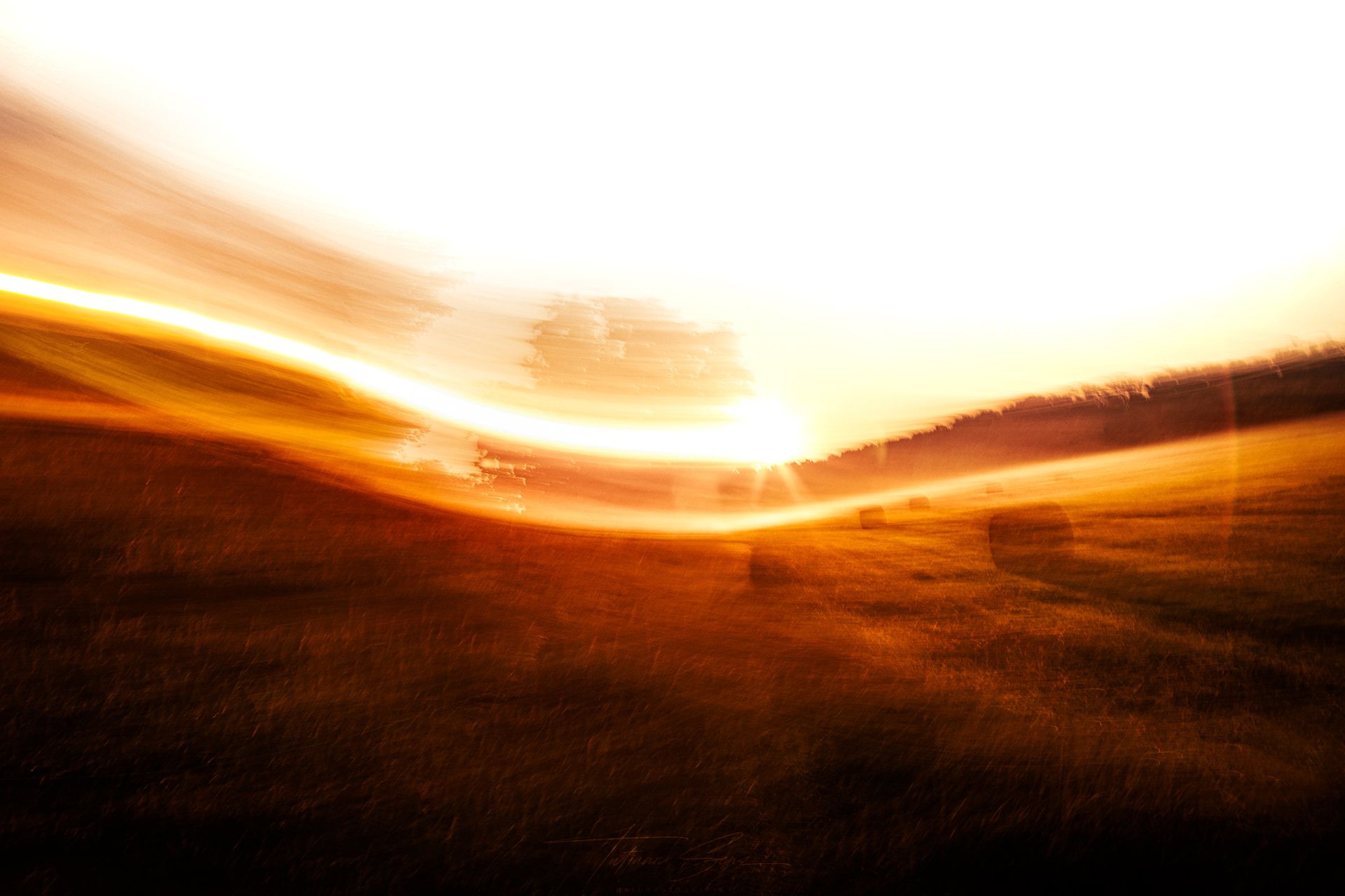 Verschwommener Sonnenuntergang über einem Feld mit orangefarbenen und weißen Lichtstreifen.