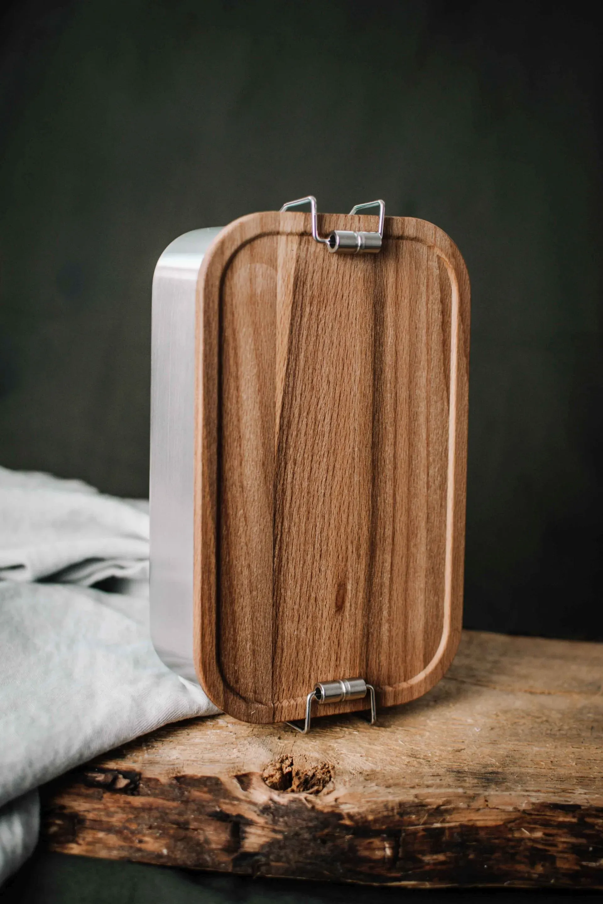 Lunchbox aus Holz und Edelstahl auf einer Holzoberfläche vor dunklem Hintergrund.