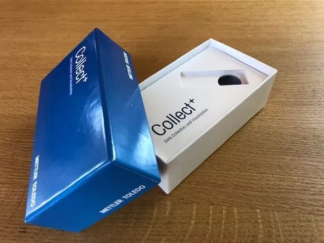 Blau-weiße Collect+-Box, eine offen, auf einer Holzoberfläche.