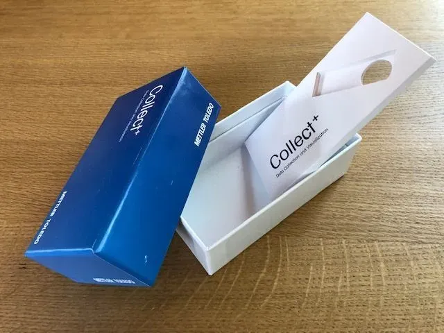 Blau-weißer Collect+ Versandkarton auf einer Holzoberfläche, teilweise geöffnet.