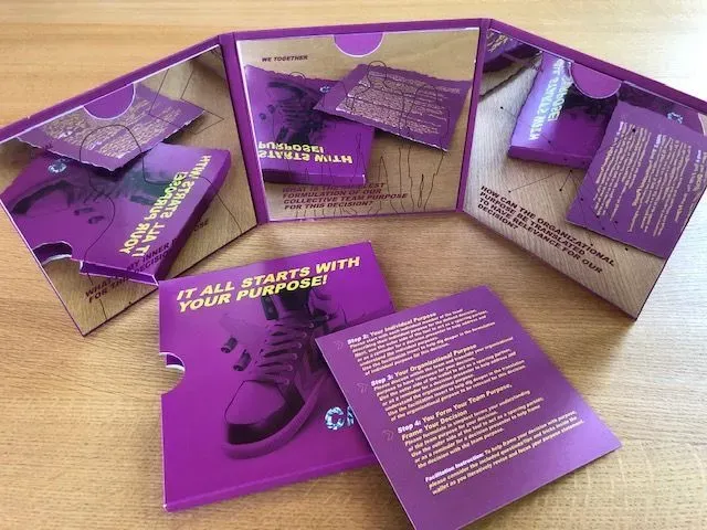 Lila gefaltete Broschüre mit Schuhgrafik, die Karten und Text enthält, auf einer Holzoberfläche.