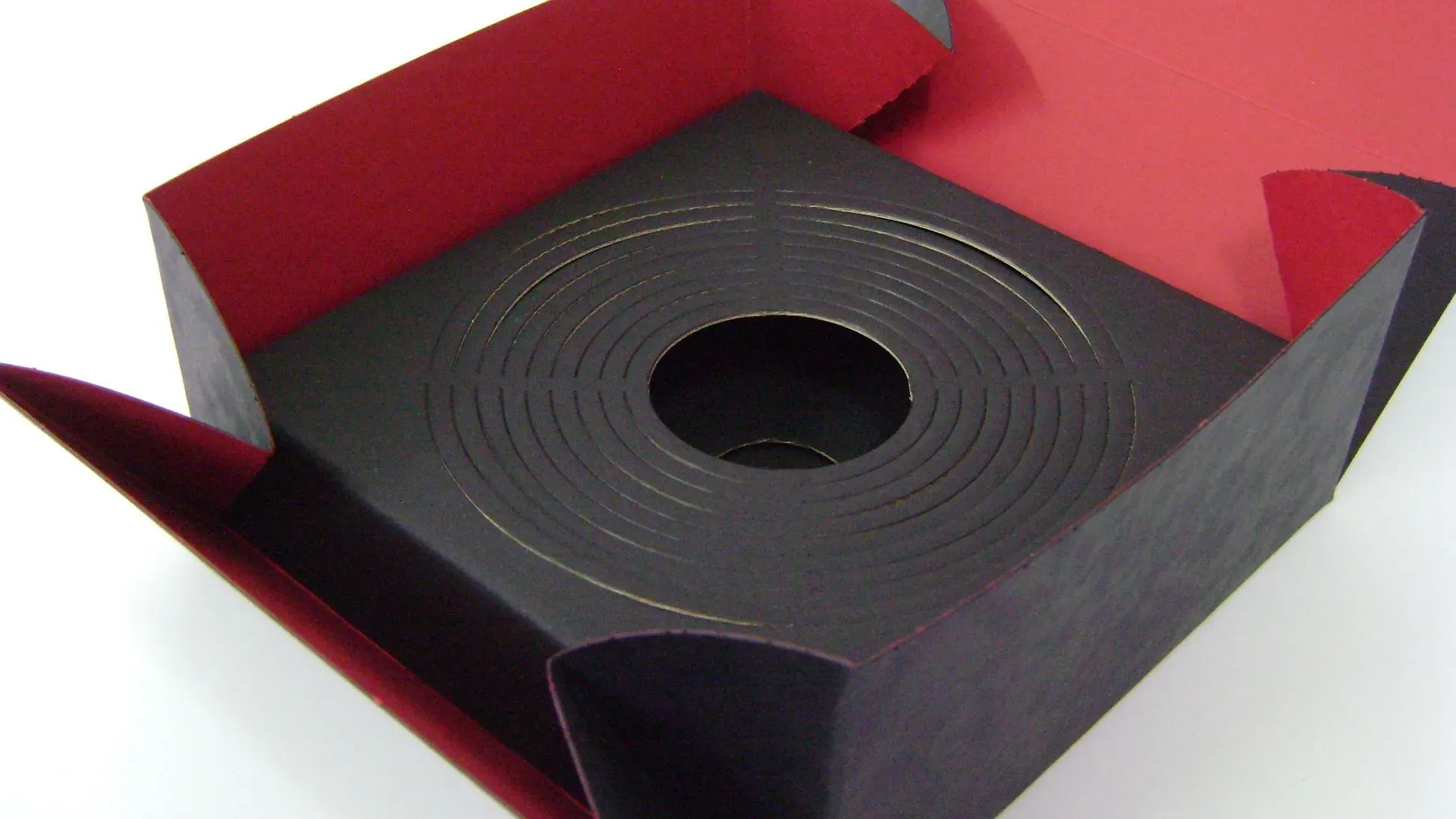 Dunkle Box mit rotem Innenraum, geöffnet, mit einer Spirale aus schwarzem Material und einem Loch in der Mitte.