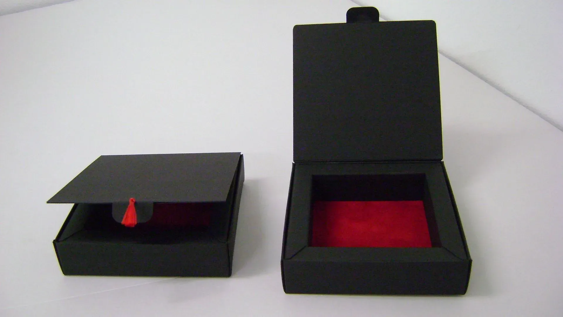 Zwei offene schwarze Schmuckschatullen mit Innenausstattung aus rotem Samt auf einer weißen Oberfläche.