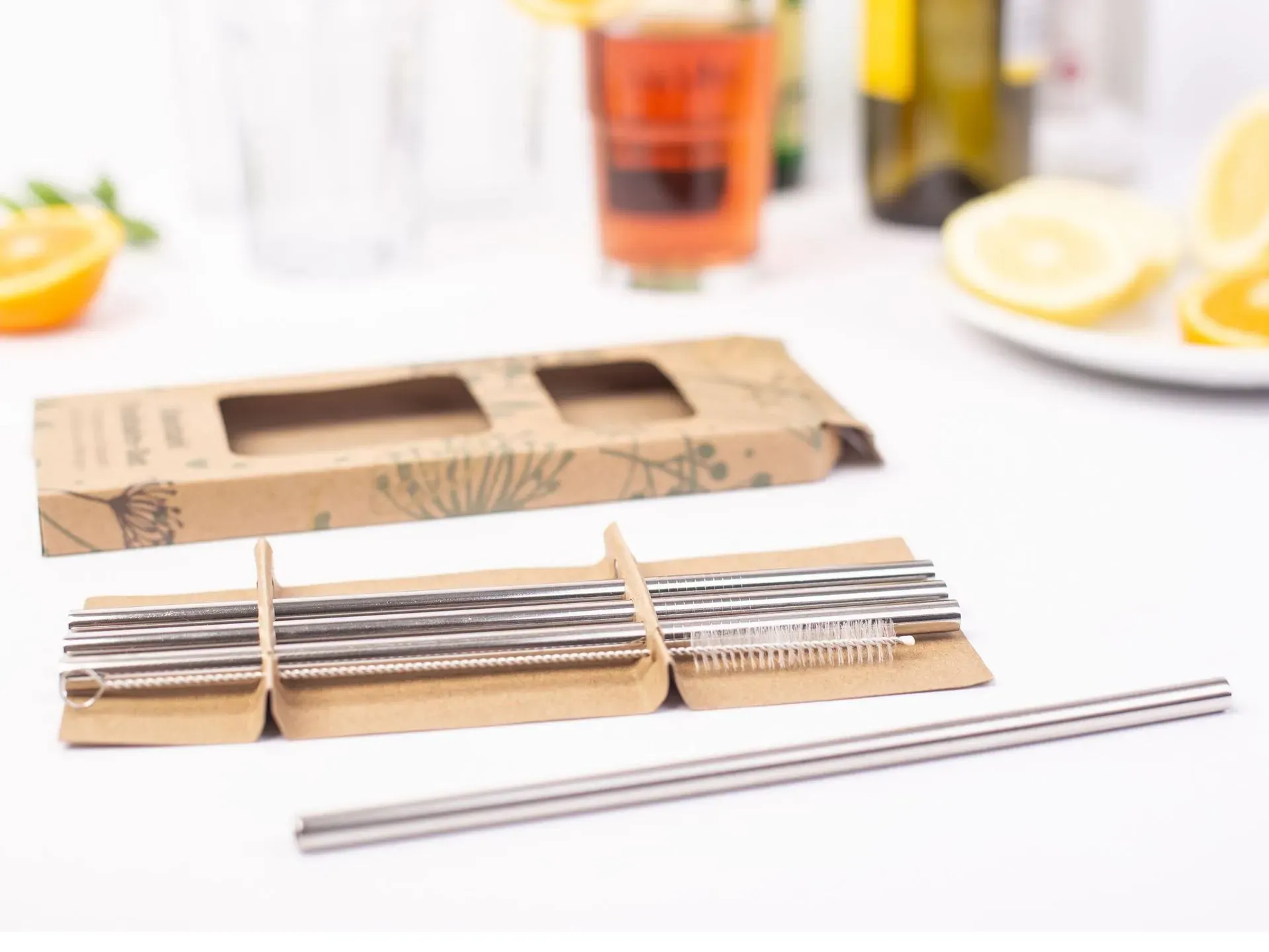 Edelstahl-Strohhalme mit Reinigungsbürste und Box, neben Getränken und Zitrone.