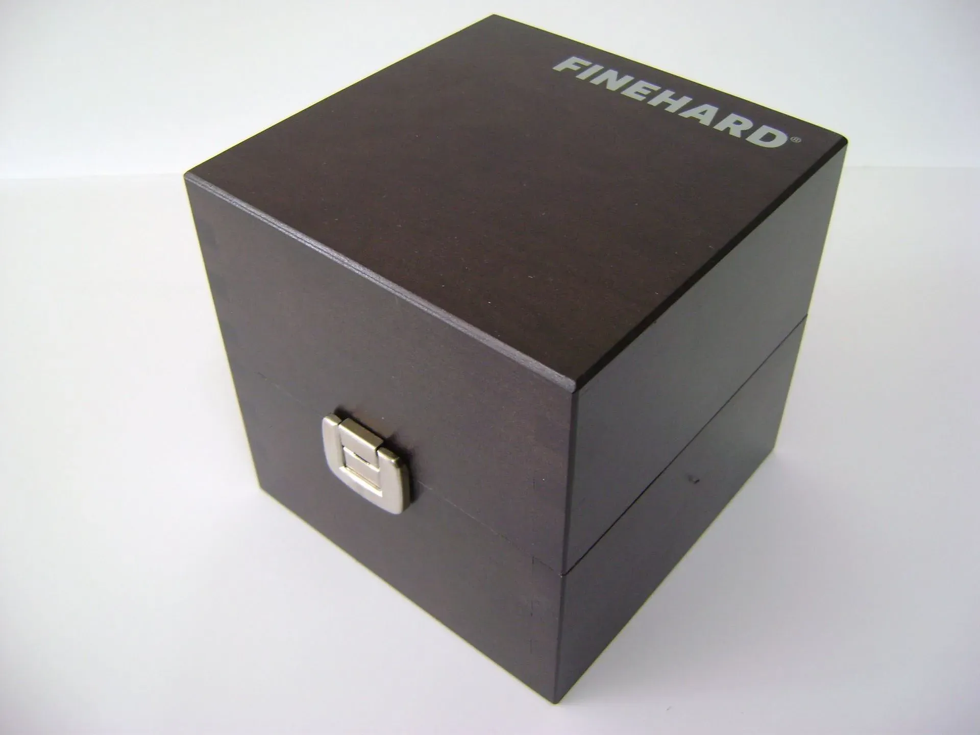 Dunkle Holzkiste mit dem Wort „FINEHARD“ auf der Oberseite. An der Vorderseite befindet sich ein silberner Verschluss.