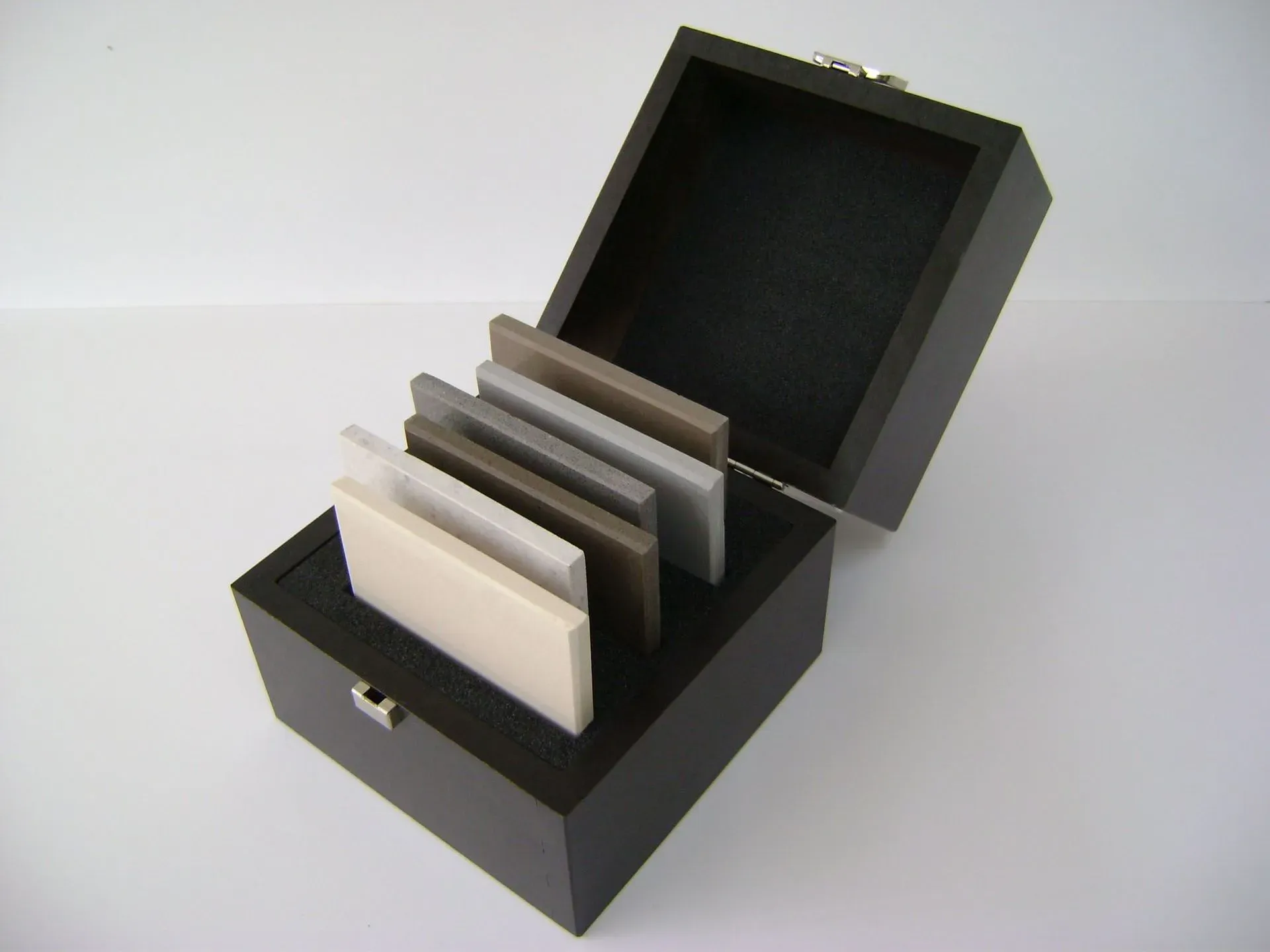 Eine dunkle Holzkiste mit mehreren darin angeordneten Farbmustern vor einem weißen Hintergrund.