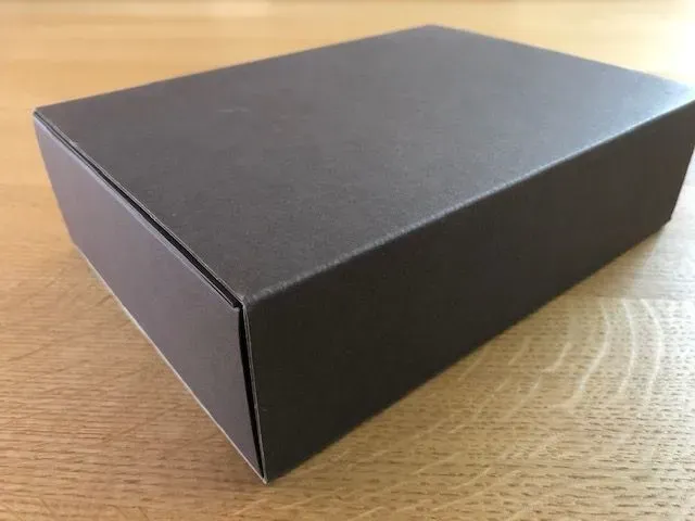 Dunkelgraue rechteckige Box auf heller Holzoberfläche.