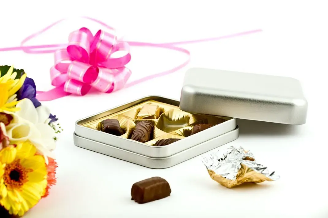 Pralinenschachtel mit Pralinen, rosa Schleife, Blumen und weißem Hintergrund.