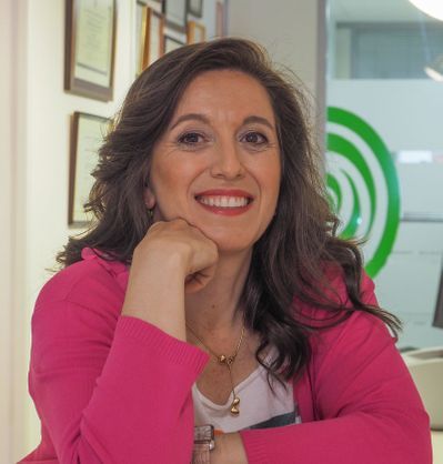 Una mujer con una chaqueta rosa sonríe con la mano en la barbilla.
