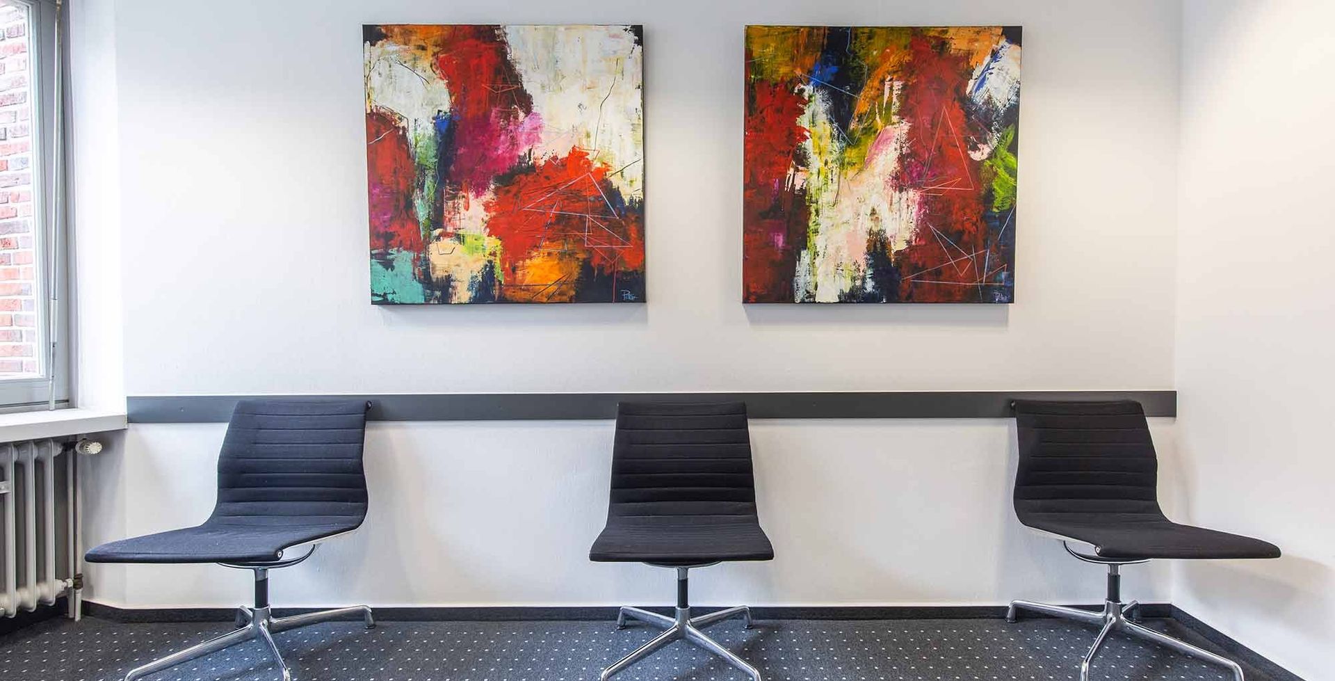Ein Wartezimmer mit drei Stühlen und zwei Gemälden an der Wand