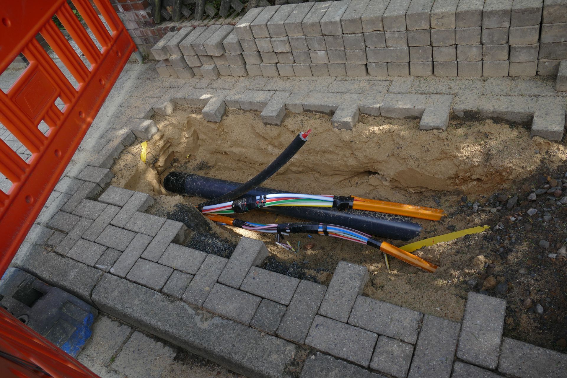 eine Reihe von Kabeln in einem Graben neben einem orangefarbenen Zaun