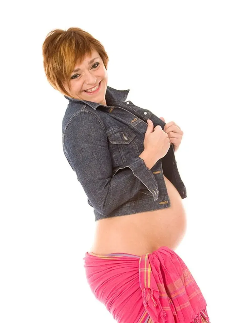 Mujer embarazada sonriendo, con chaqueta vaquera y pareo rosa.