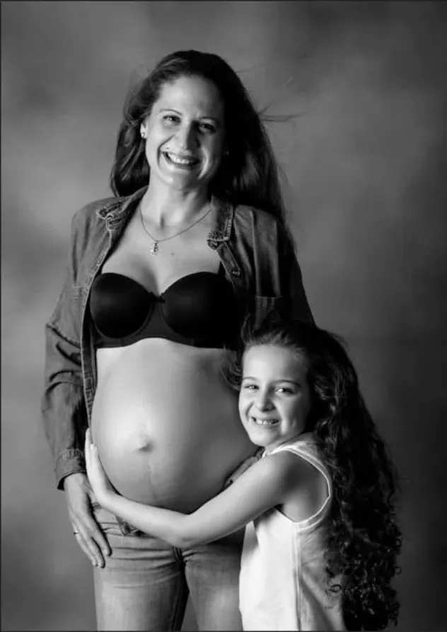 Mujer embarazada en sujetador y chaqueta, con su hijo abrazando su vientre, sonriendo en el estudio.