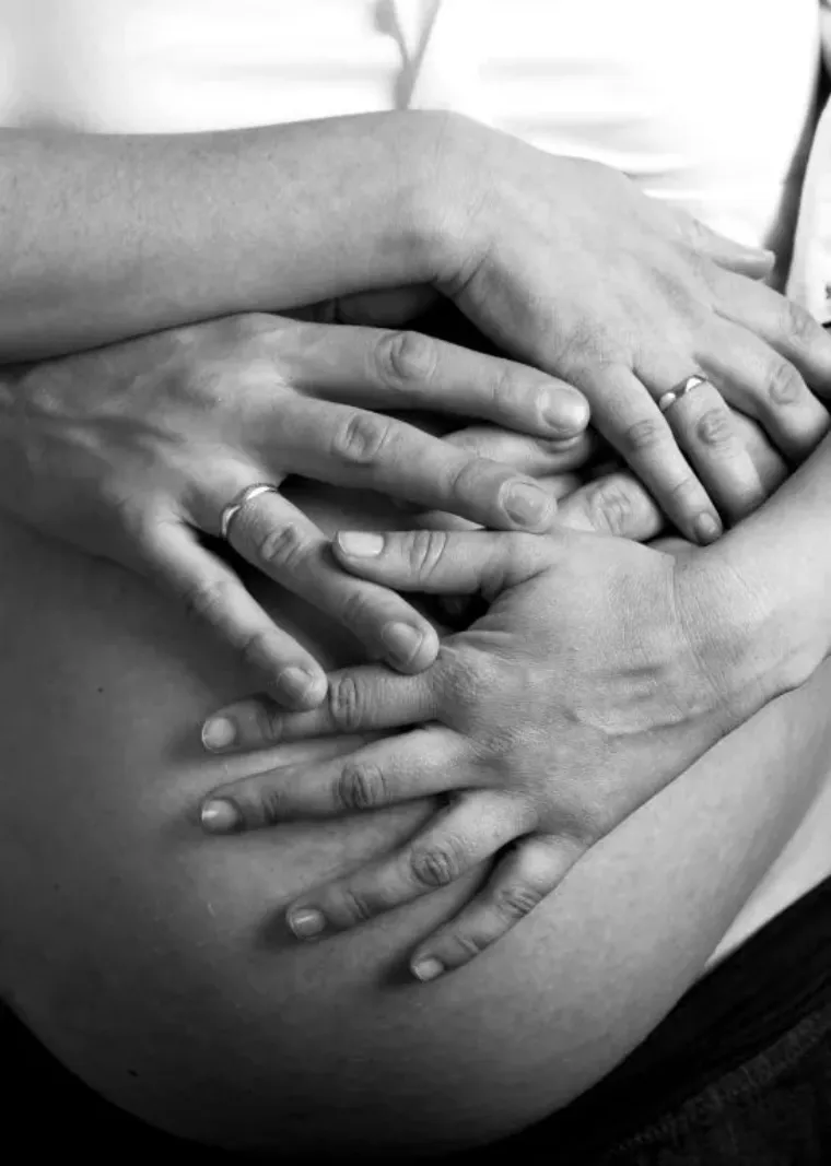 Unas manos acarician un vientre de embarazada. Un par de manos llevan anillos. Blanco y negro.