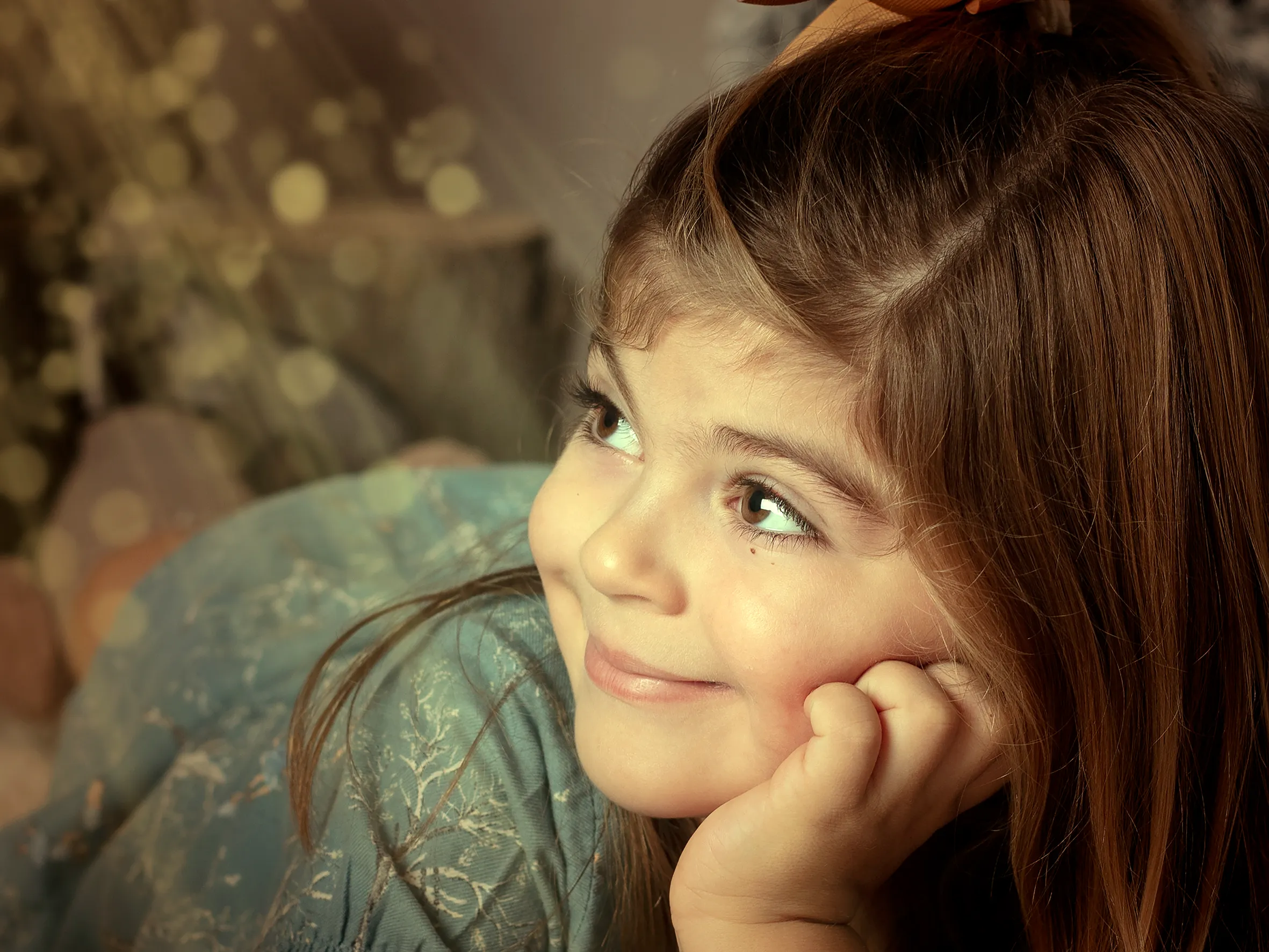 Una chica de pelo castaño mira hacia arriba sonriendo. Se lleva la mano a la barbilla. Fondo desenfocado con efecto bokeh dorado.