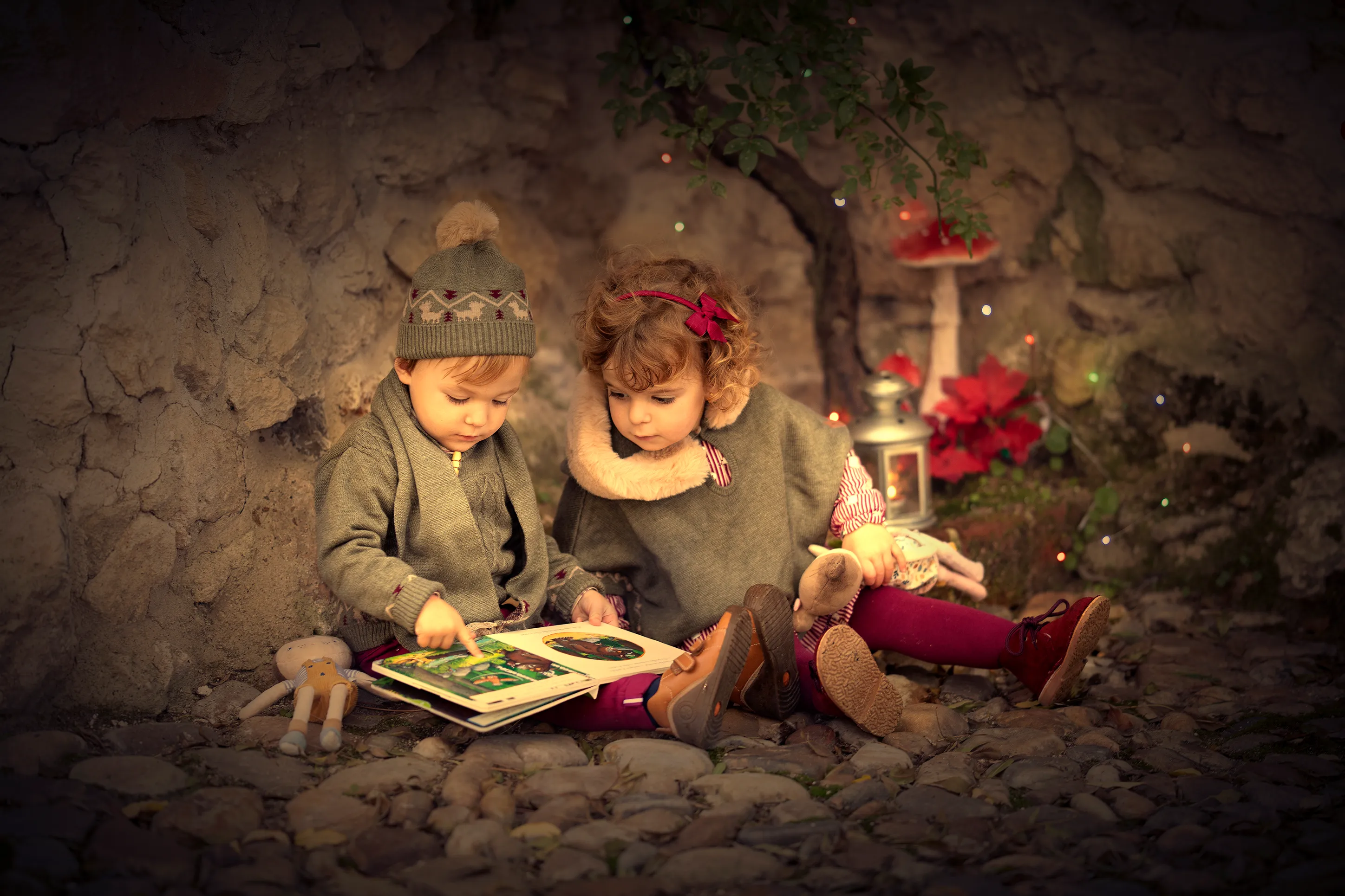 Dos niños leen un libro en una cueva; uno señala la página.
