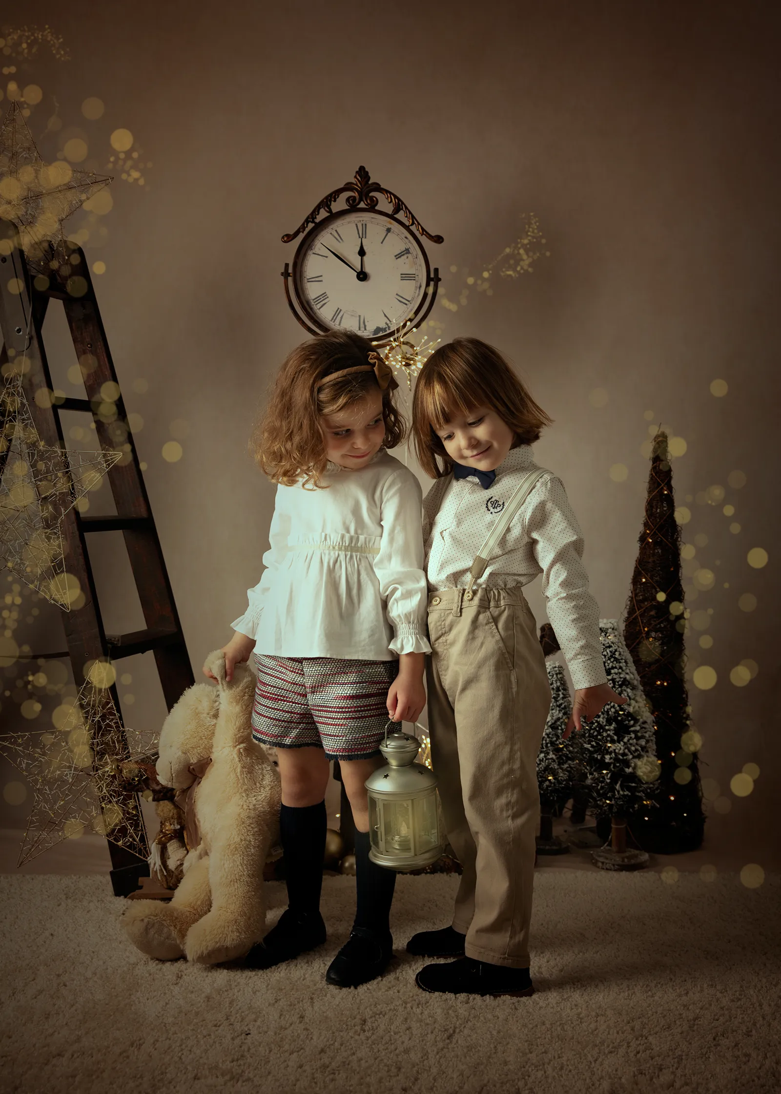 Dos niños mirando una linterna en un ambiente festivo, con un reloj encima, una escalera y un osito de peluche presentes.