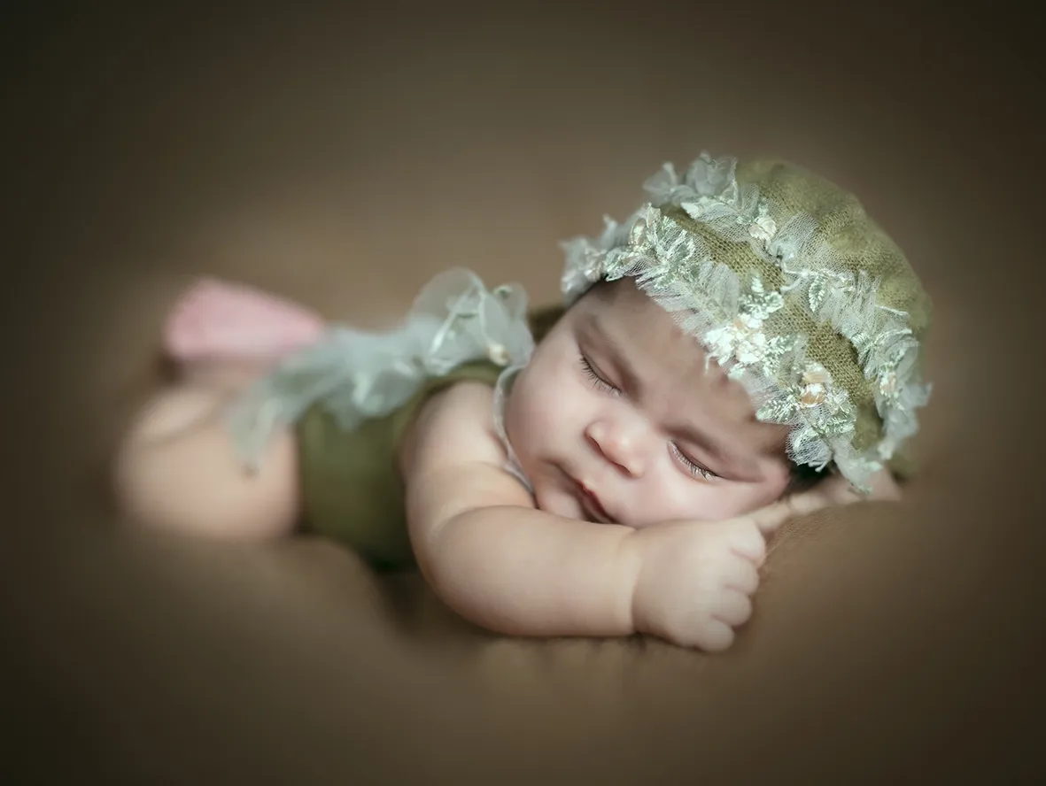 Bebé dormido con un gorro de encaje, tumbado sobre una superficie marrón.