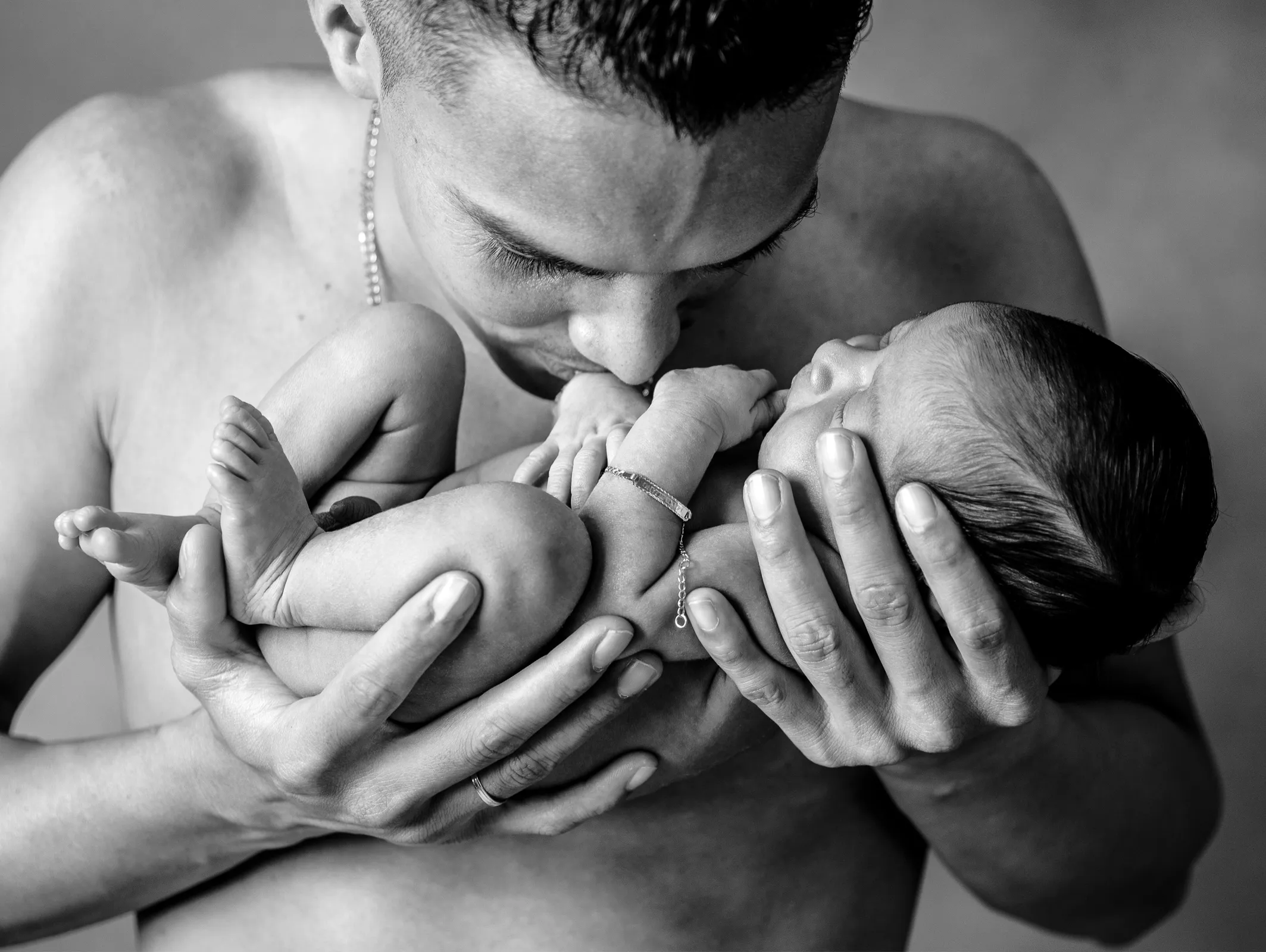 Una persona sostiene y besa a un bebé recién nacido, ambas imágenes en blanco y negro.