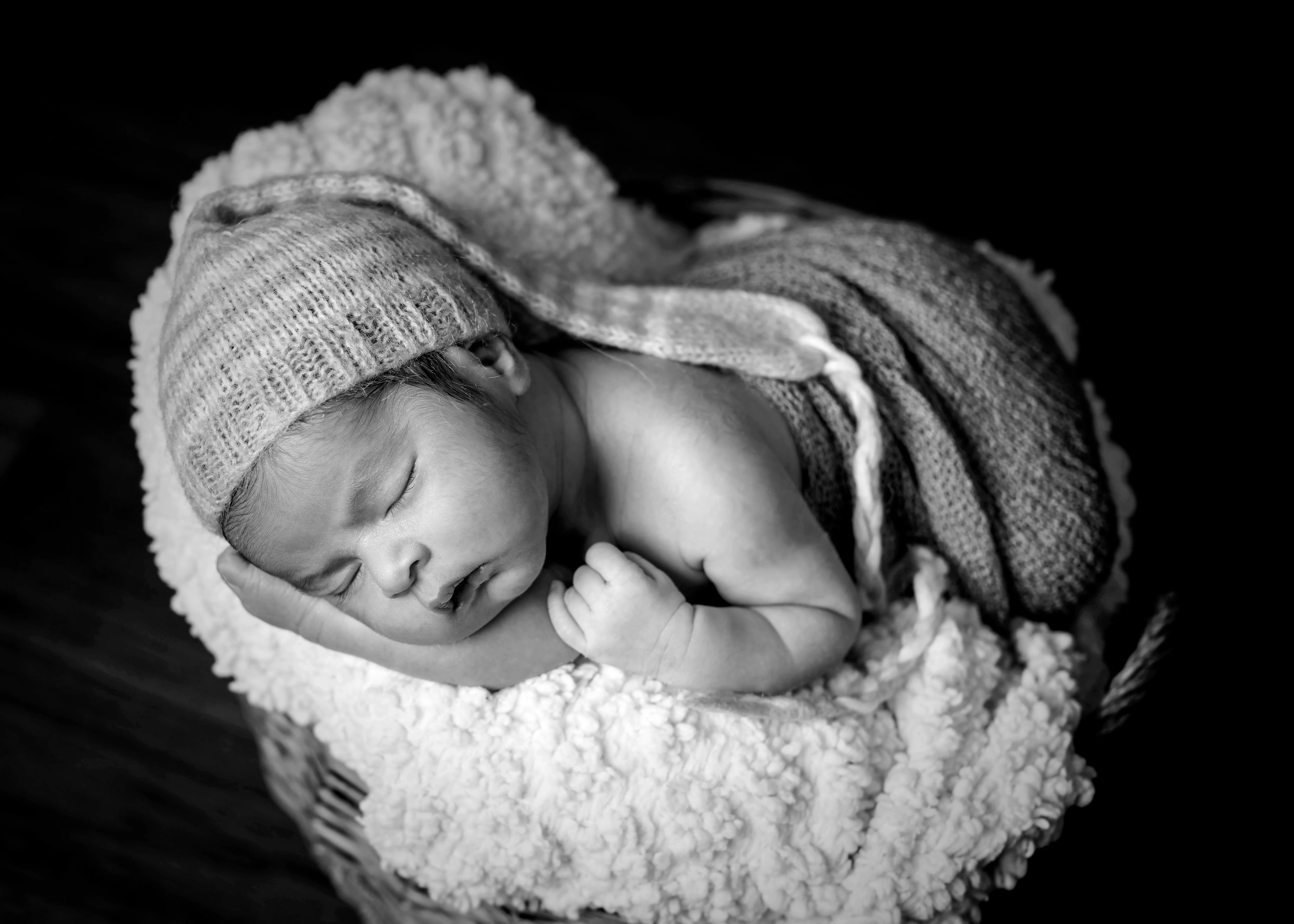 Bebé recién nacido durmiendo en una cesta, con un gorro de lana. Blanco y negro.