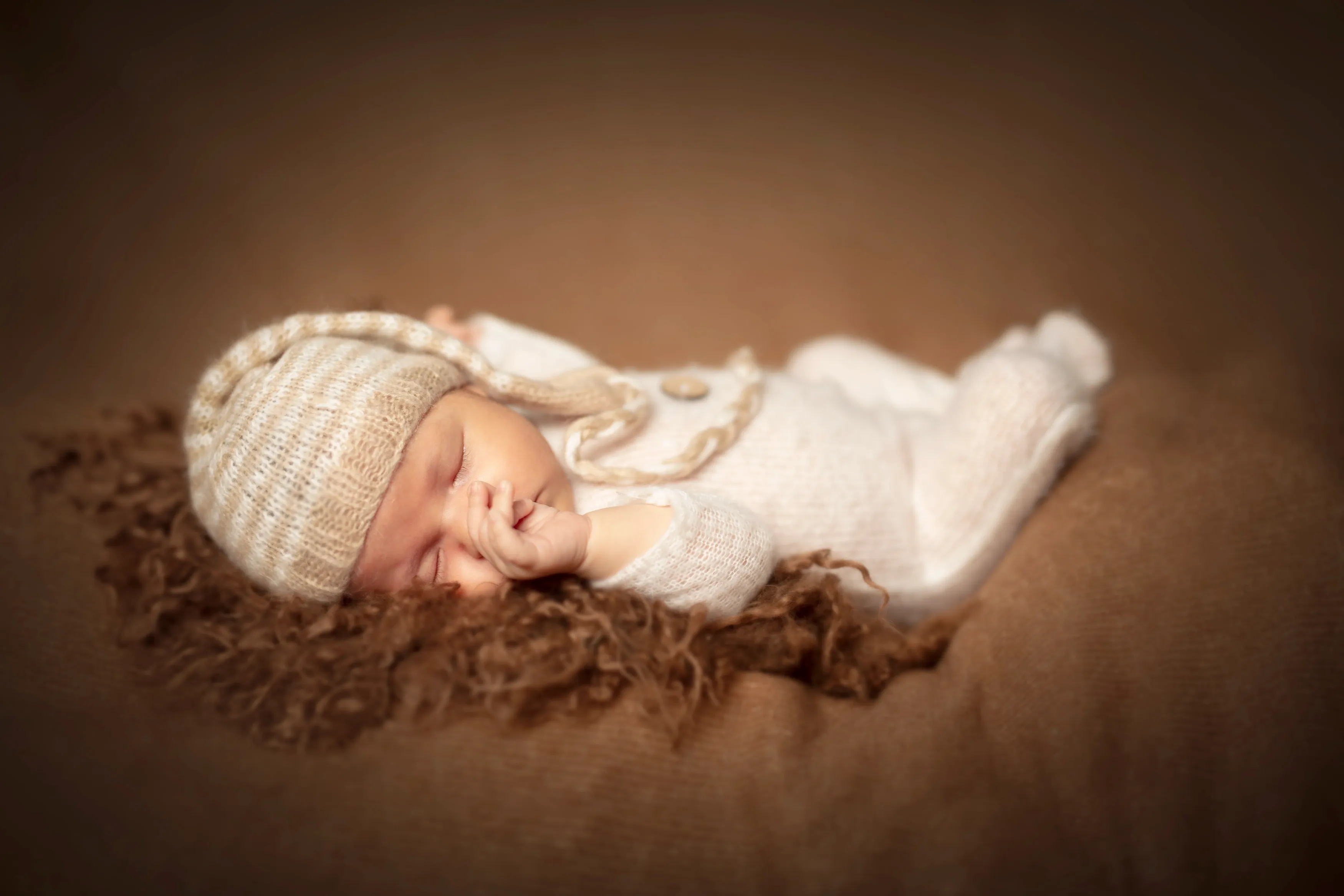 Bebé recién nacido durmiendo, con gorro y conjunto de punto, sobre piel marrón.