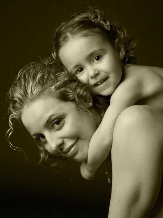 Mujer con un niño a la espalda, ambos sonriendo. Fotografía de estudio en tonos sepia sobre fondo oscuro.