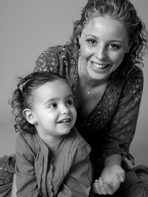 Una mujer sonríe mientras mira a un niño pequeño. El niño sonríe y mira hacia un lado. Ambos tienen el pelo rizado.