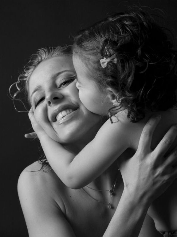 Madre sonríe mientras el niño le besa la mejilla, primer plano, blanco y negro.