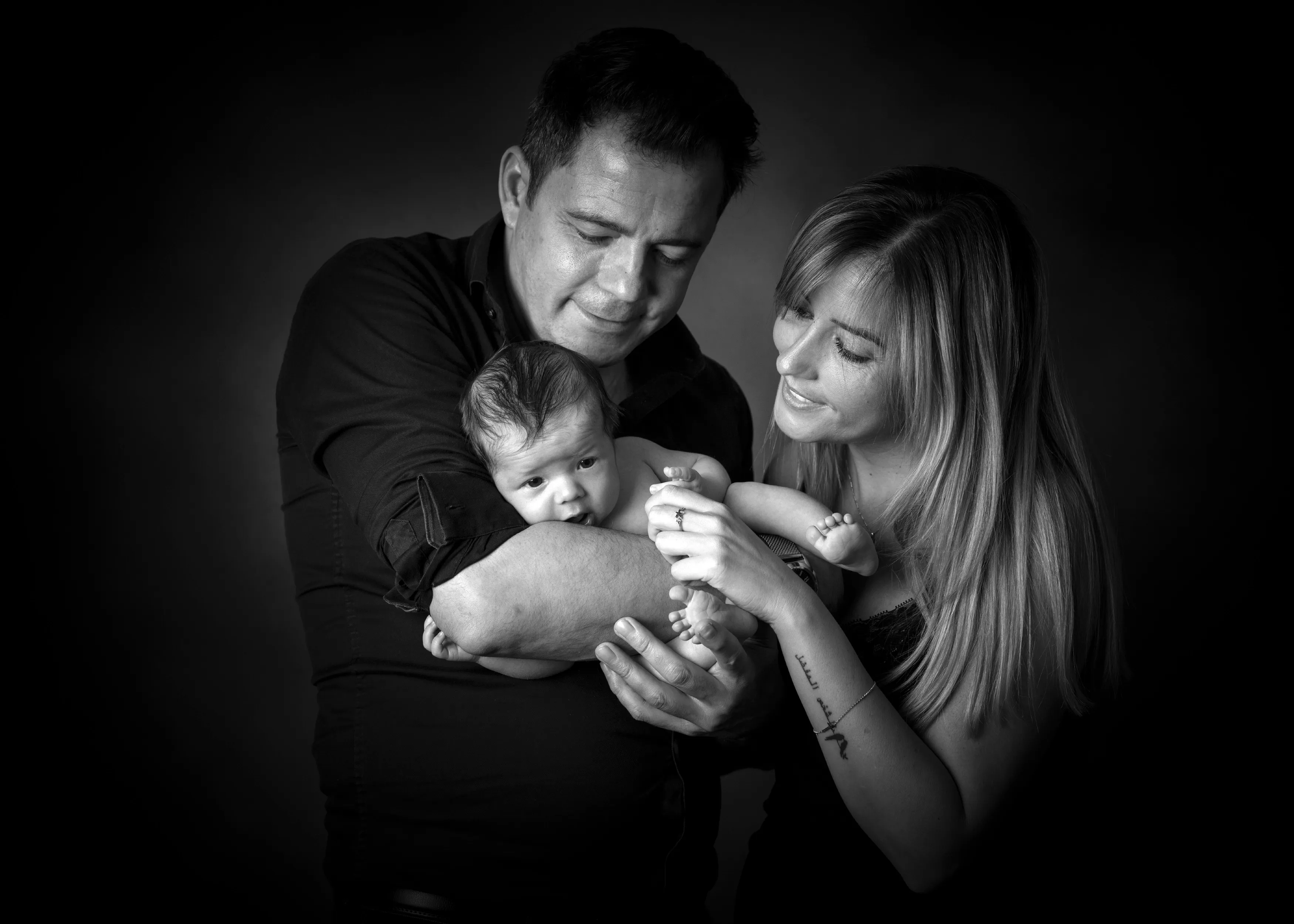 Padres acunando a un recién nacido; retrato en blanco y negro.