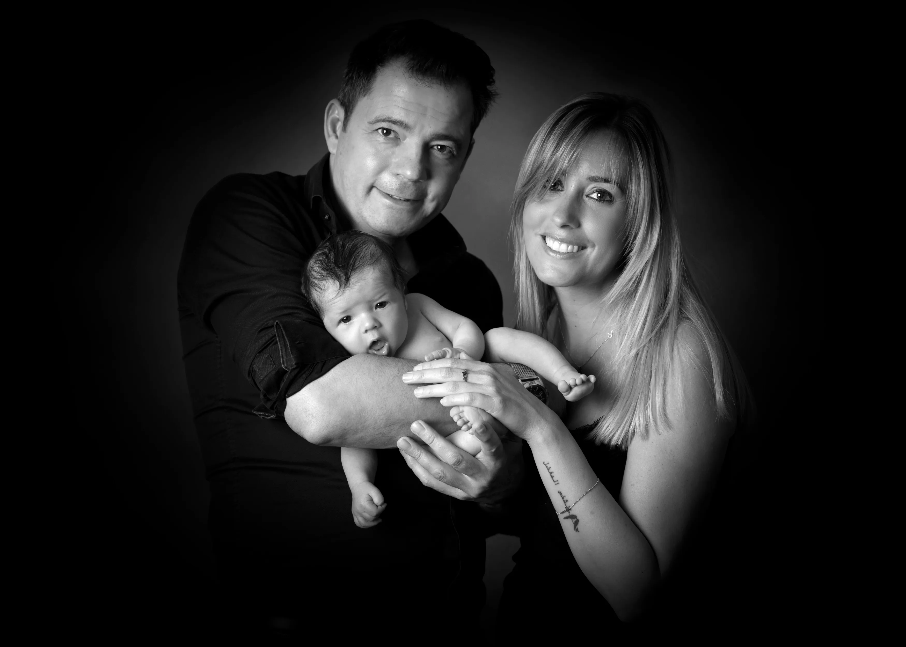 Padres sonrientes sosteniendo a su bebé recién nacido. Retrato de estudio en blanco y negro.