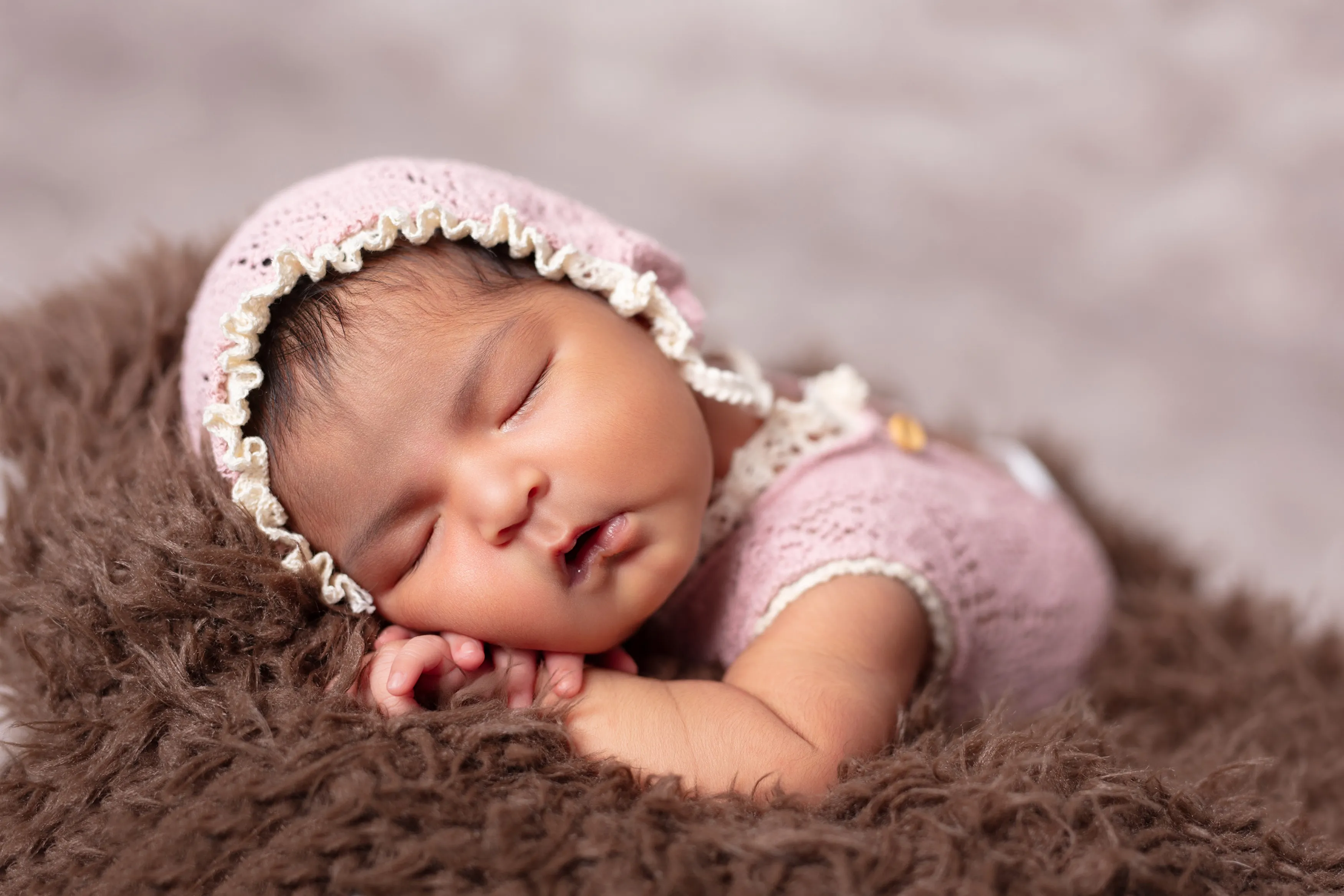 Bebé durmiendo con un gorrito y un conjunto rosa, descansando sobre una suave manta de piel marrón.