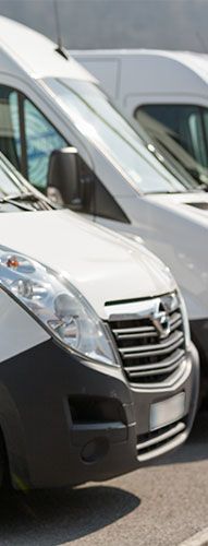 Des camionnettes blanches garées les unes contre les autres sur un parking, avec un gros plan de l'avant de l'un d'elles.