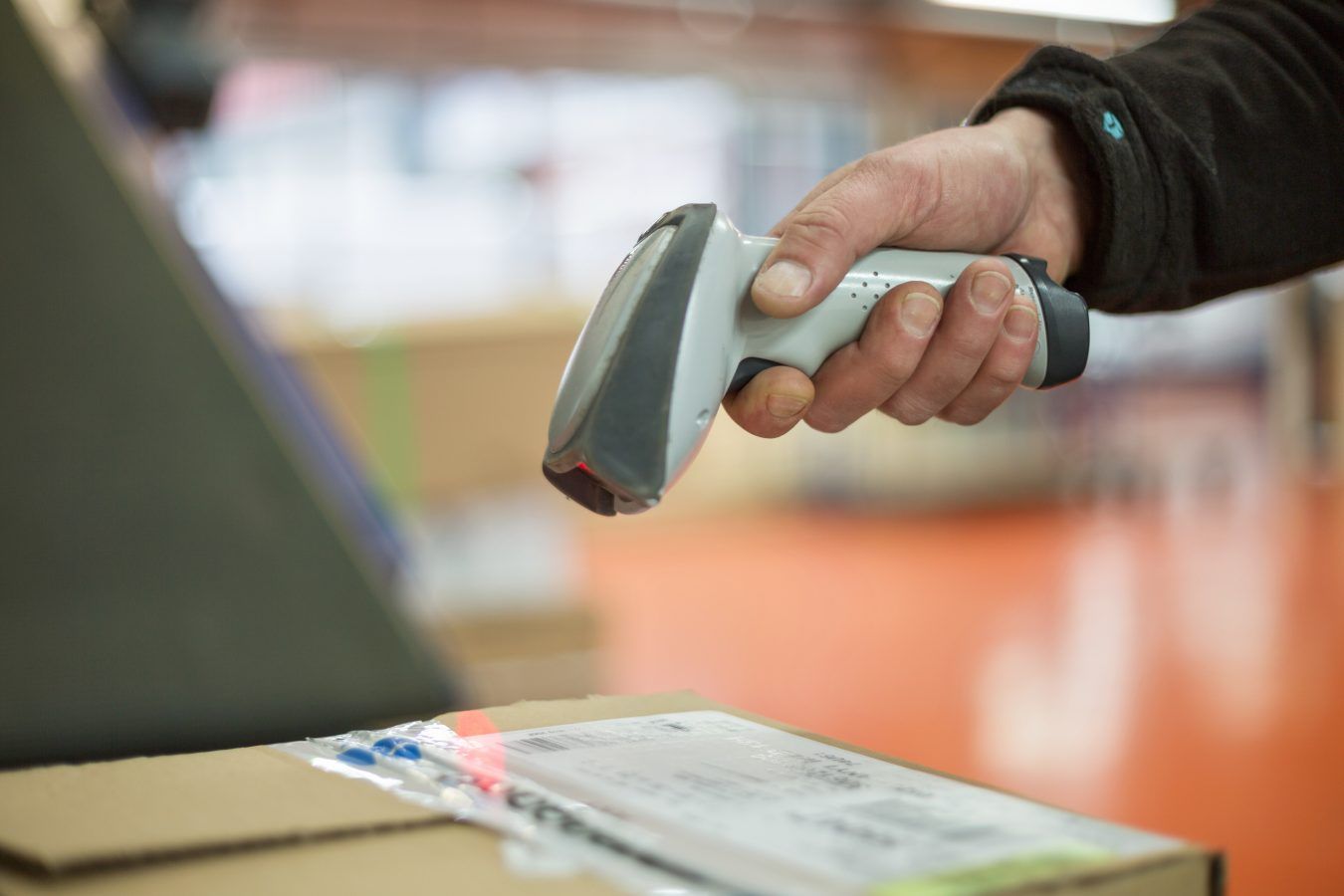 Main tenant un lecteur de codes-barres portable au-dessus d'un colis sur un tapis roulant