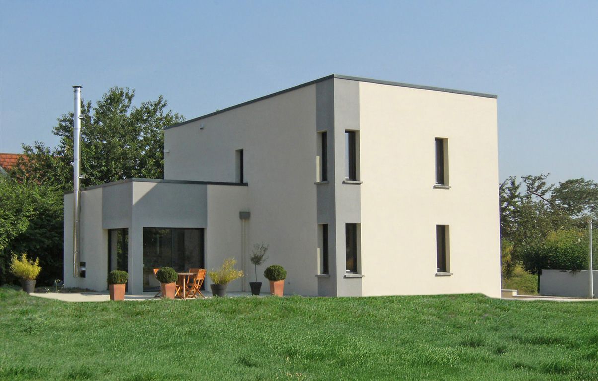 Maison moderne à deux étages avec des murs de couleur claire, des accents gris et de petites fenêtres rectangulaires.